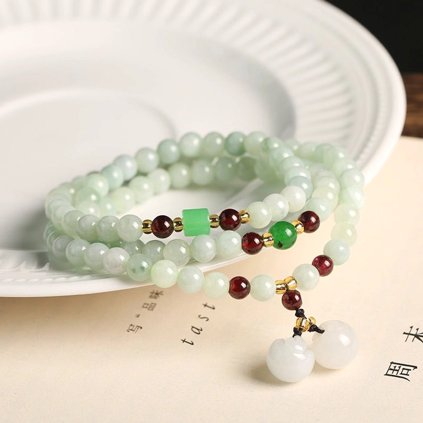 Multi-strand jade bracelet with round white jade pendants and red-green spacer beads on white plate with book page background