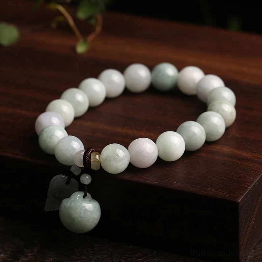 Genuine jade apple pendant bracelet with gradient off-white to light green beads and round jade charm on wooden display with botanical elements