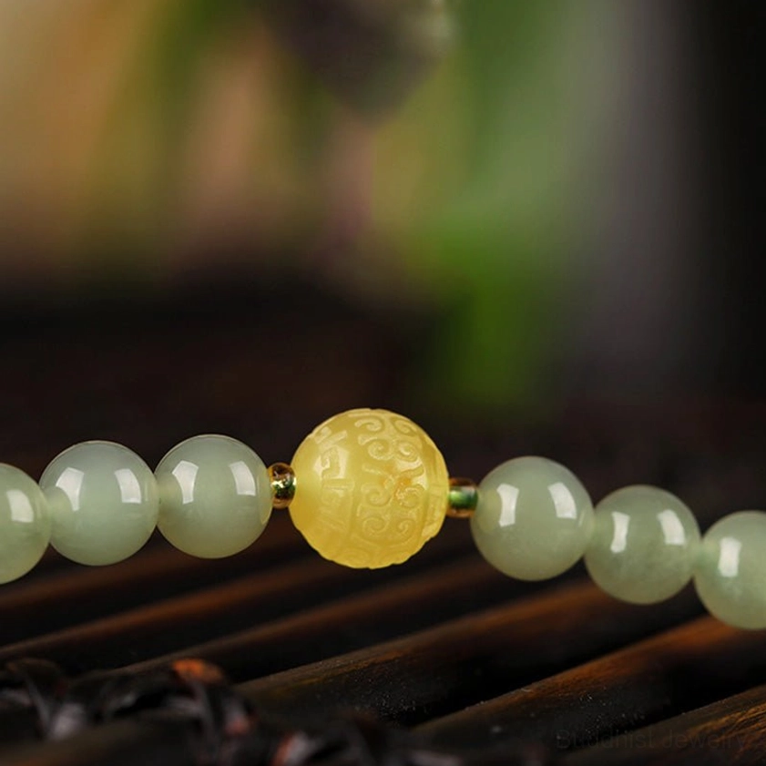 Macro detail of jade 108-bead strand showing round light green jade beads and carved amber decorative spacer bead