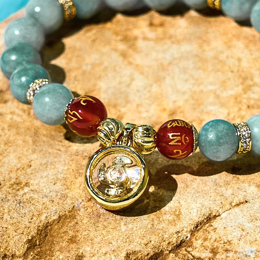Close-up view of jade mantra bracelet displaying clear engraved gold spinning charm with Om Mani Padme Hum symbols and carved red bead details