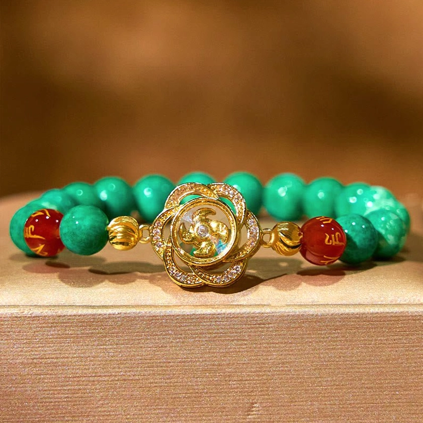 Sacred mantra bracelet with jade beads and gold cyclone charm on wooden surface