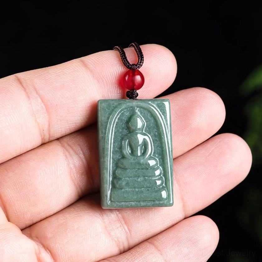Jade Buddha amulet pendant with oblique side profile, displaying embossed relief carving against dark background with red bead cord