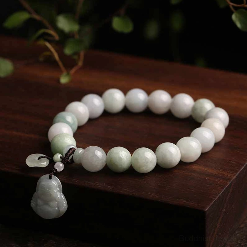 Handmade jade Buddha bracelet with pale pink and light green beads, jade figurine and leaf pendants on dark wooden surface with green foliage
