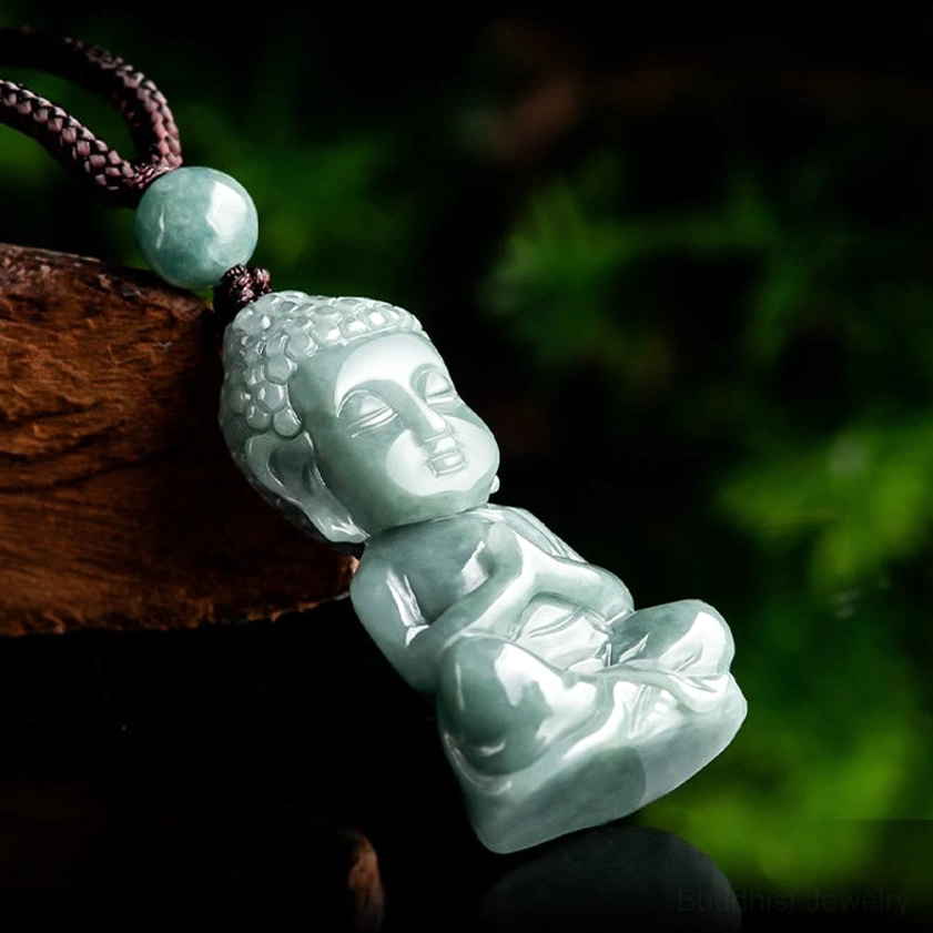 Side angle view of jade Buddha pendant lying horizontally, showing the serene face and compact carved details on natural jade stone