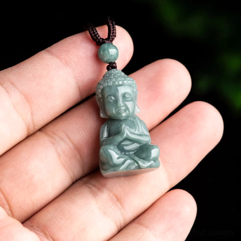 Jade Buddha pendant held in human palm, showing compact miniature size and hand-carved details in natural jade stone