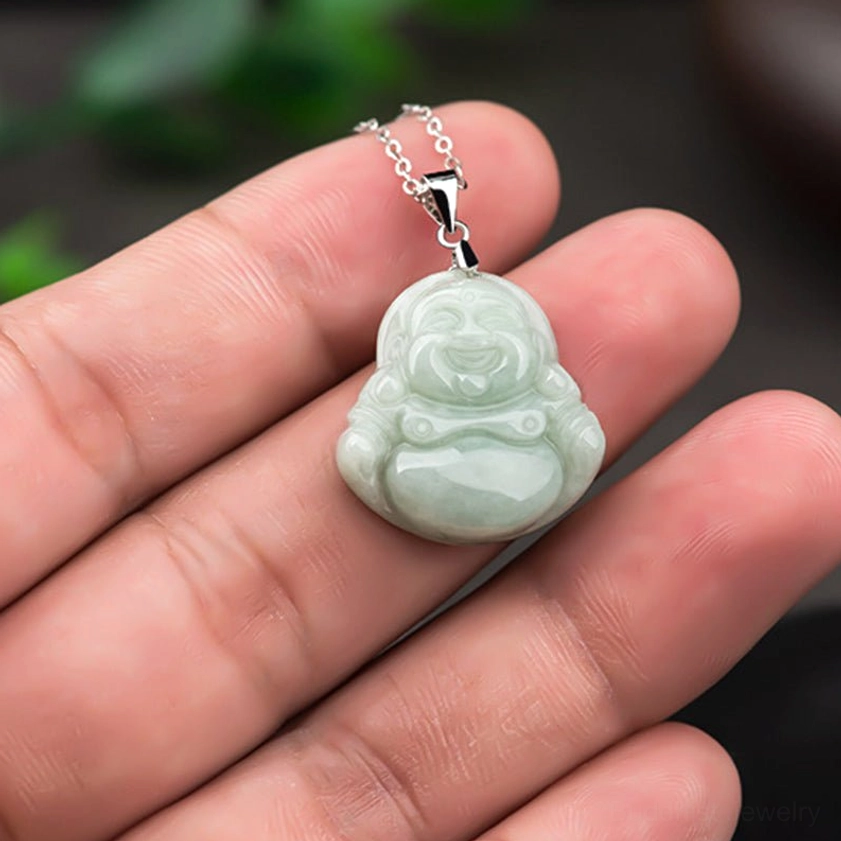 Small jade Laughing Buddha pendant held in human hand eye-level shot demonstrating miniature size pale green jade with silver chain and buckle