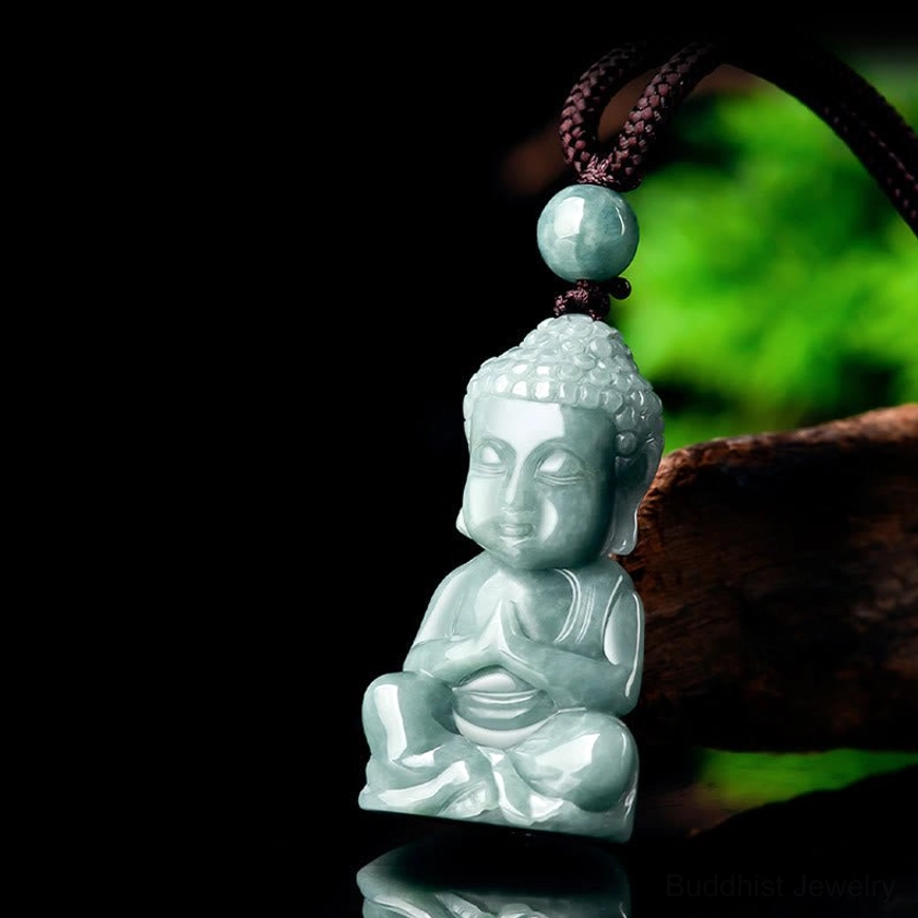 Three-quarter view of jade Buddha meditation pendant reflected on glossy surface, displayed on wooden prop showing carved details