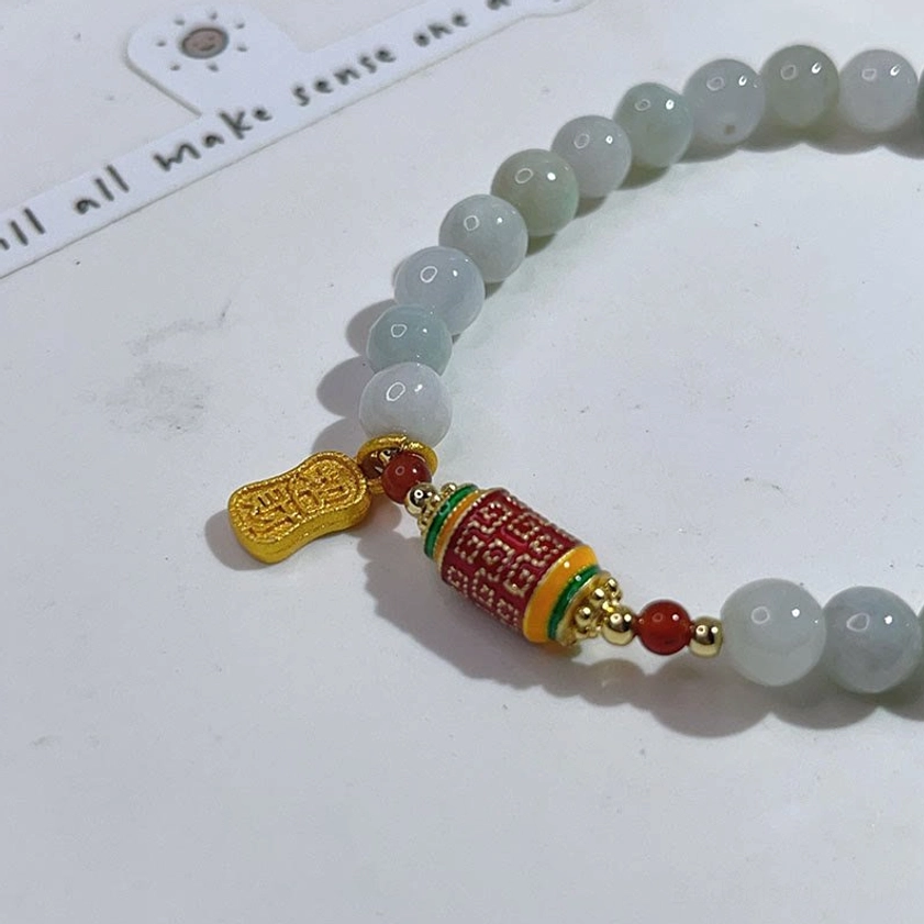 Close-up detail of light jade prayer wheel bracelet showing smooth beads and gold Fu drop pendant