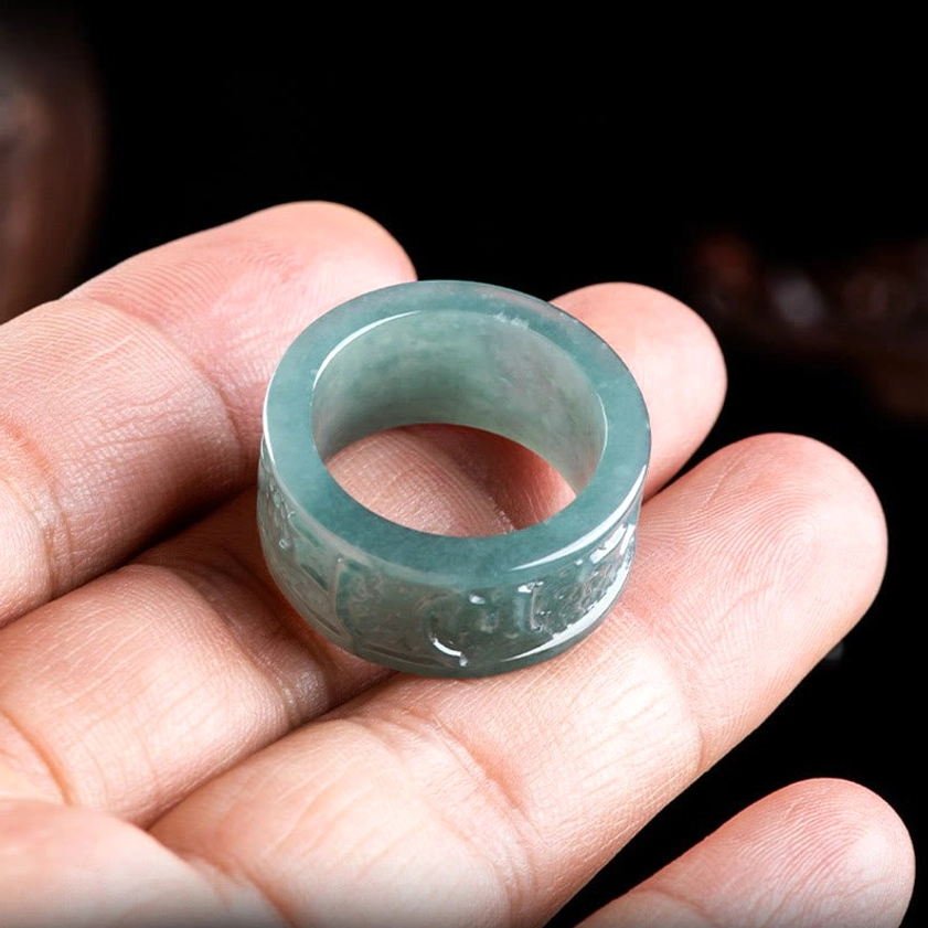 Carved jade Buddhist ring lying flat on palm, profile view showing ring thickness, width, and detailed hand-engraved mantra patterns for prosperity and protection