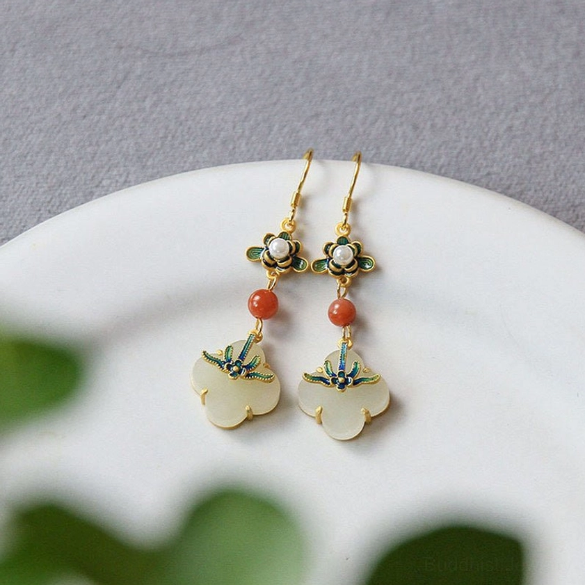 Overhead flat lay of jade four-leaf clover earrings pair on white plate with green plant backdrop