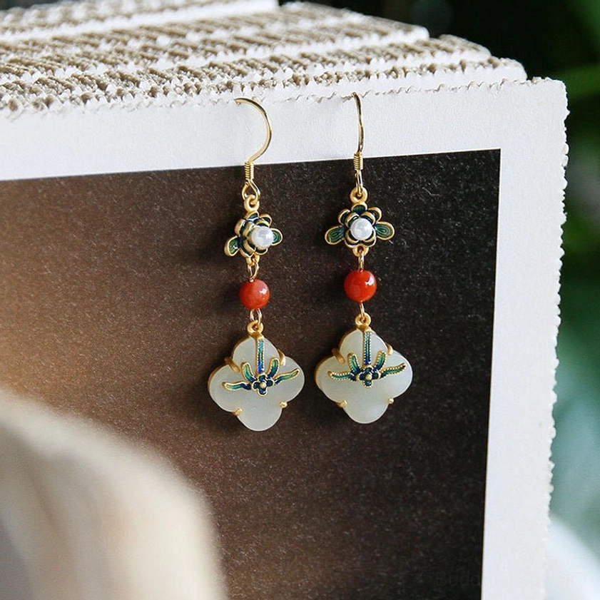 Front view of jade four-leaf clover drop earrings with pearl-decorated enamel flower and gold hooks on postcard background