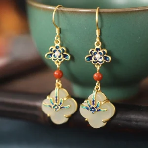 Jade four-leaf clover drop earrings with gold hooks and enamel flower details, displayed with vintage ceramic vessel