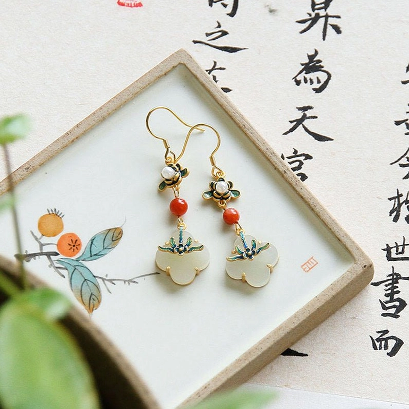 Front flat view of jade four-leaf clover drop earrings with enamel flower top and red bead on calligraphy background