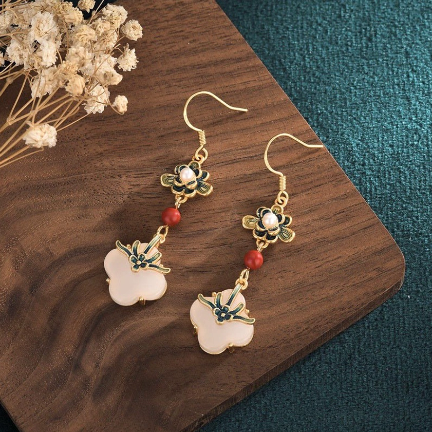 Overhead view of jade clover earrings on wooden tray with dried flowers, showing gold metal and red bead accents
