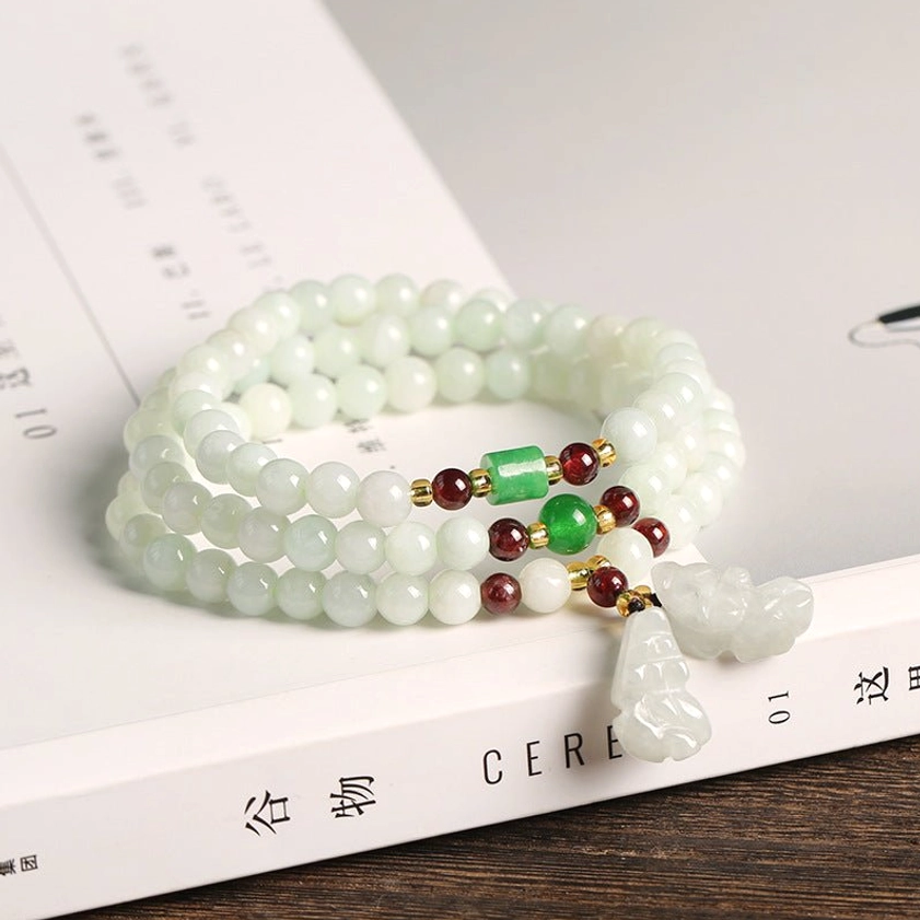 Jade gourd pendant bracelet displayed on book and wooden table, showing light green beads, red and green metal spacers, and gourd charm detail