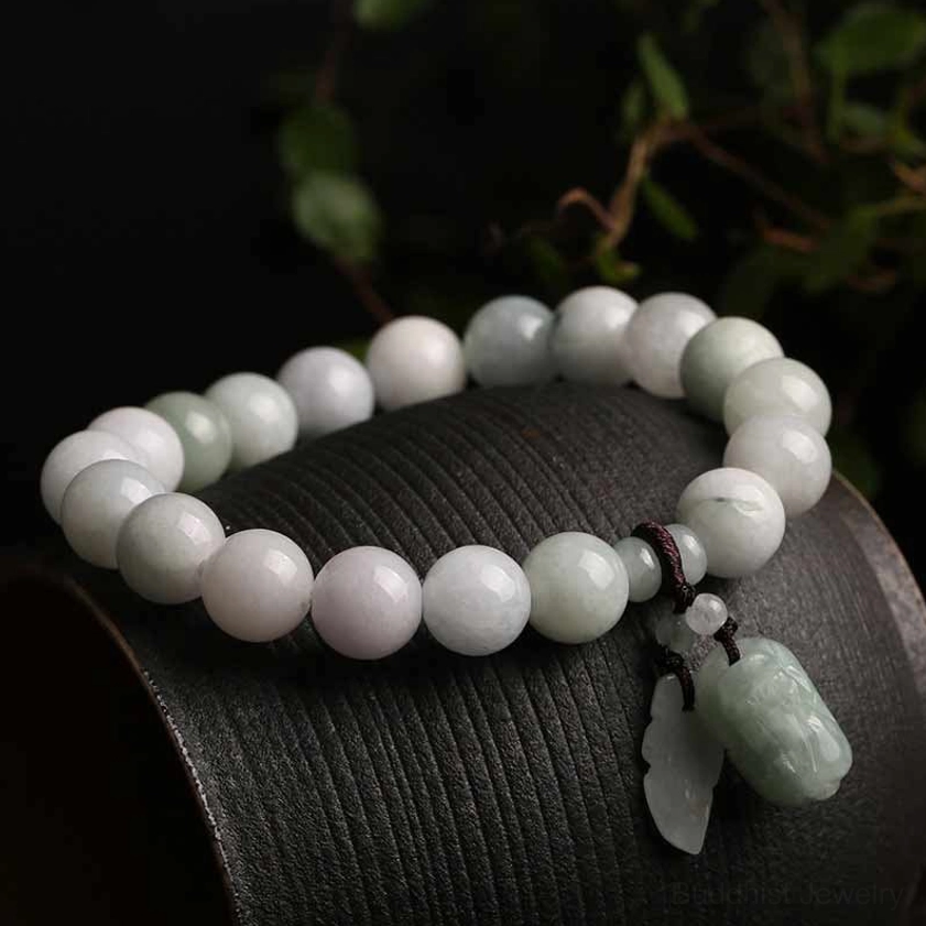 Natural jade gourd pendant bracelet with pale purple and light green jade beads on black leather wrist rest with foliage backdrop