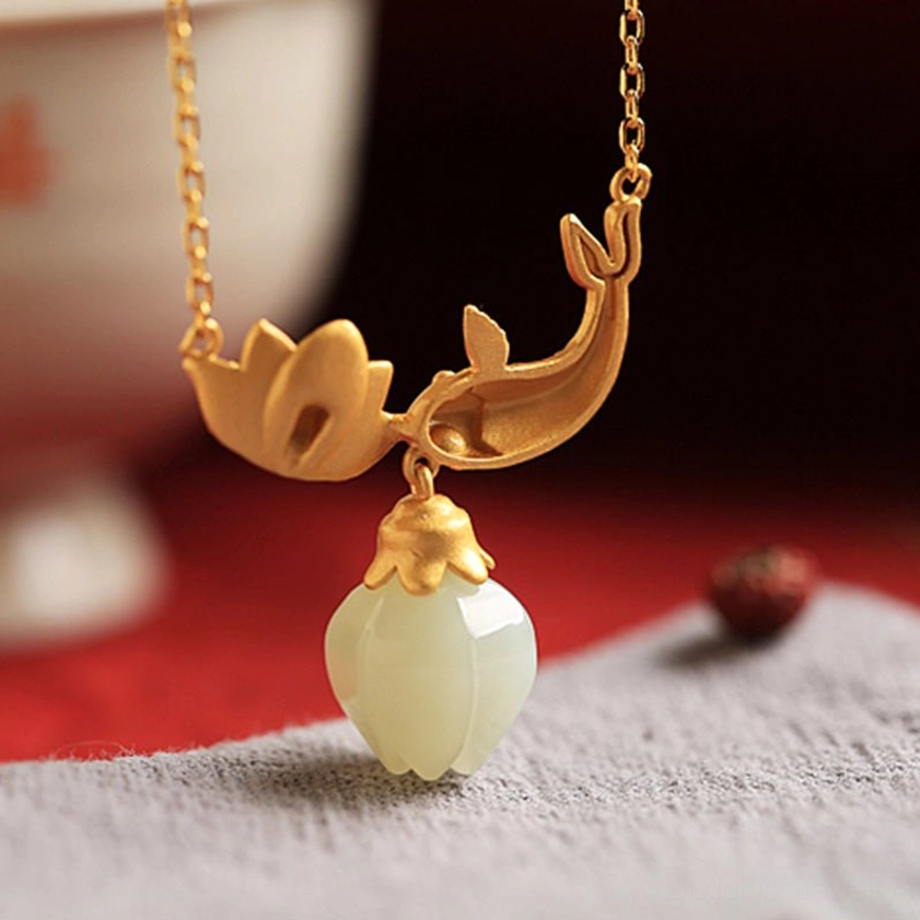 Solid gold hardware koi fish lotus jade Buddhist pendant necklace overhead view on porcelain decorative table with red cloth