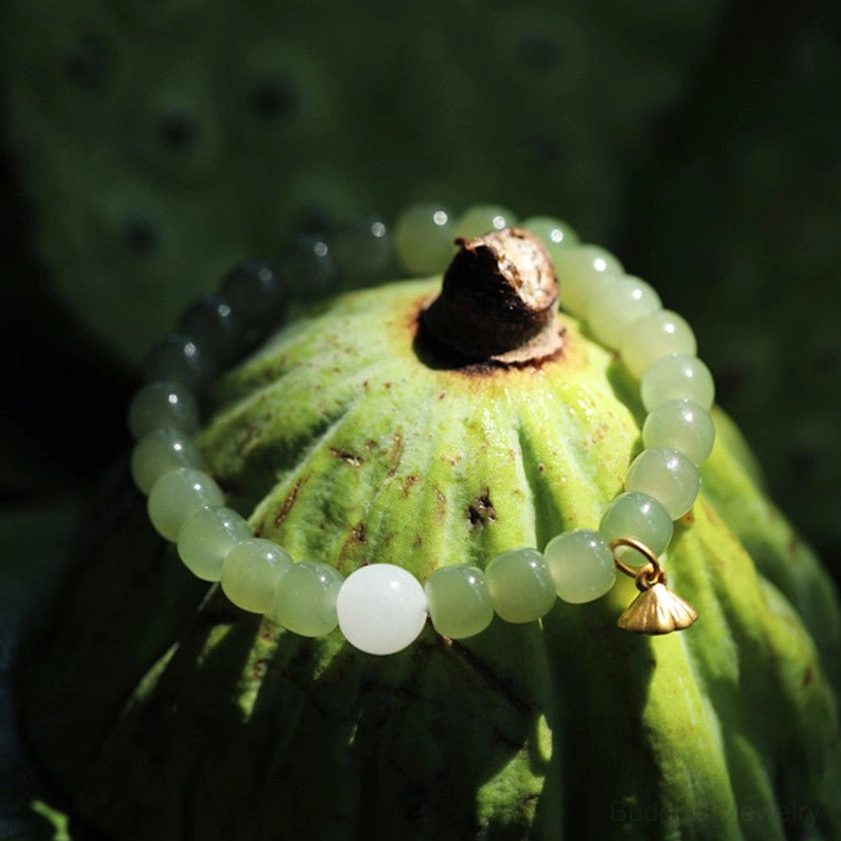 Jade beaded bracelet with gold lotus seed pod charm on green lotus leaf background