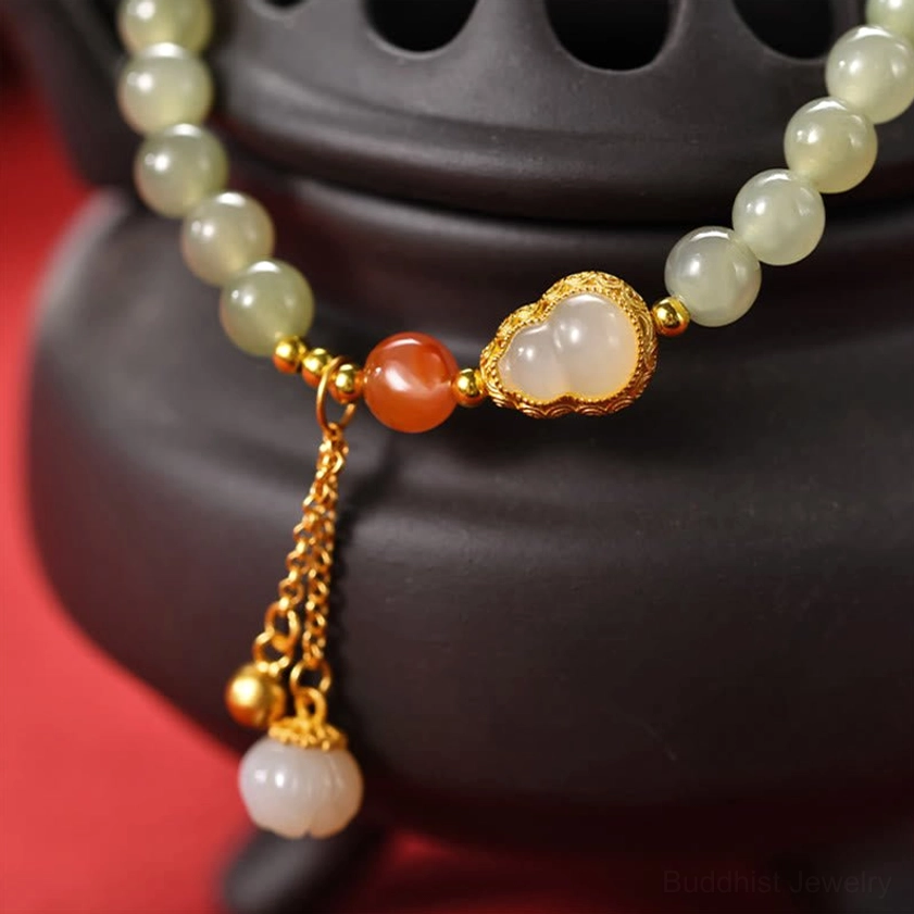 Close-up detail of hetian jade lotus charm bracelet with gold tassel and red agate accent