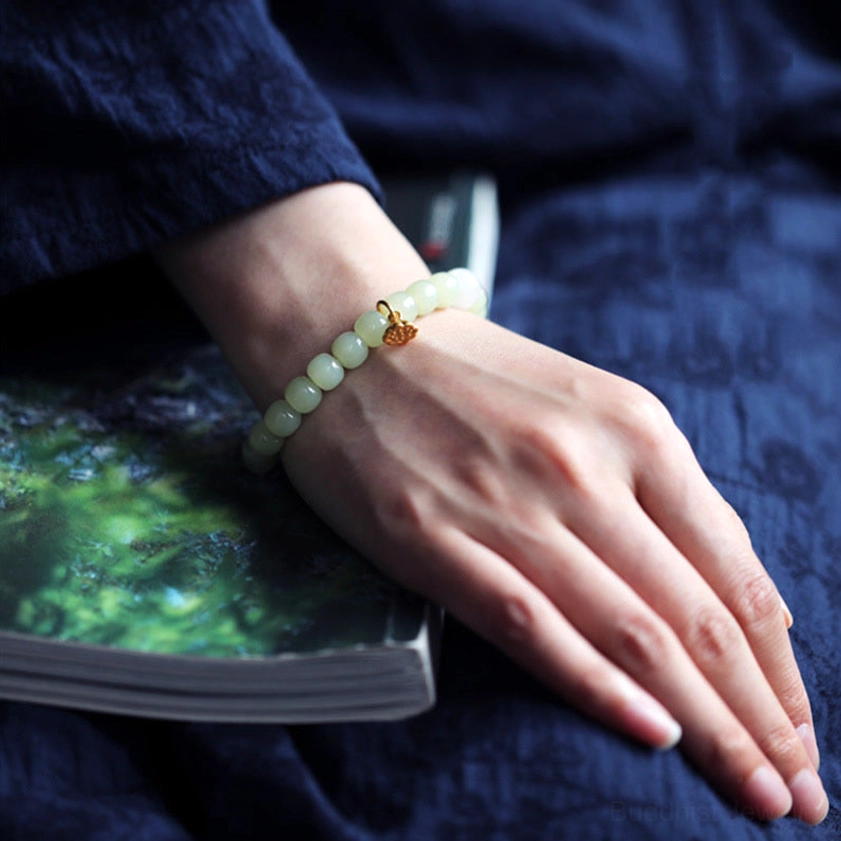 Green jade bracelet with gold lotus charm worn on left wrist against book background