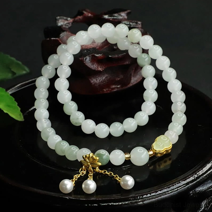 Natural jade lotus bracelet with white pearl charms and gold accents on wooden display base with green leaf prop