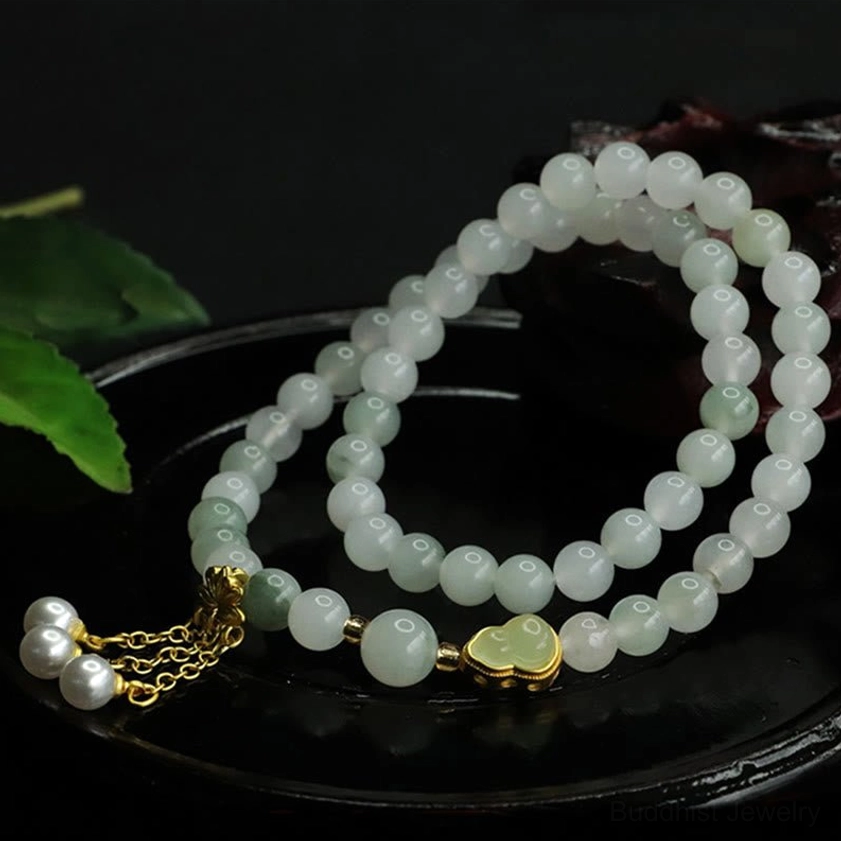 Jade lotus bracelet side view showing pale beads, gold lotus clasp, and metal chain with decorative beads on black ceramic base