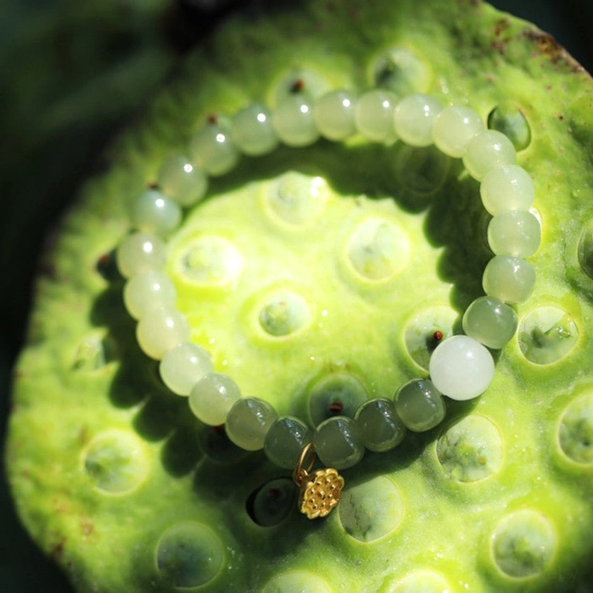 Green and white jade beads with gold lotus seed charm inside lotus pod background