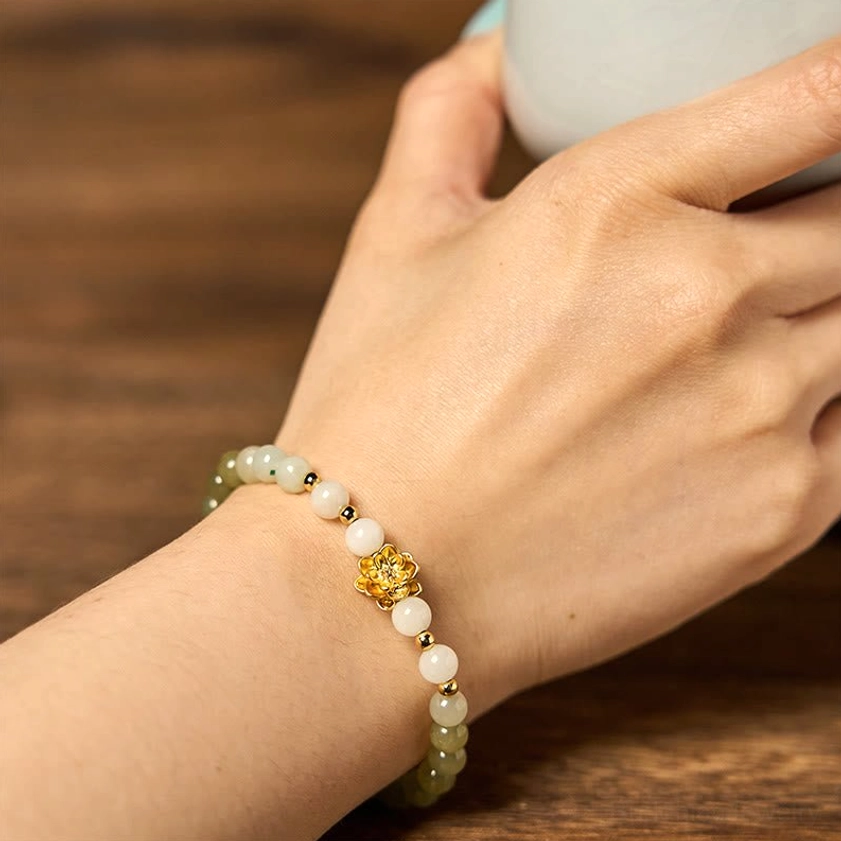 Slim Hetian jade gradient lotus bracelet on wrist next to white cup, displaying 8mm round beads and elegant gold lotus charm