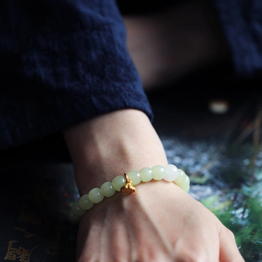 Jade lotus bracelet worn on left wrist, side view showing bead texture and gold lotus accent