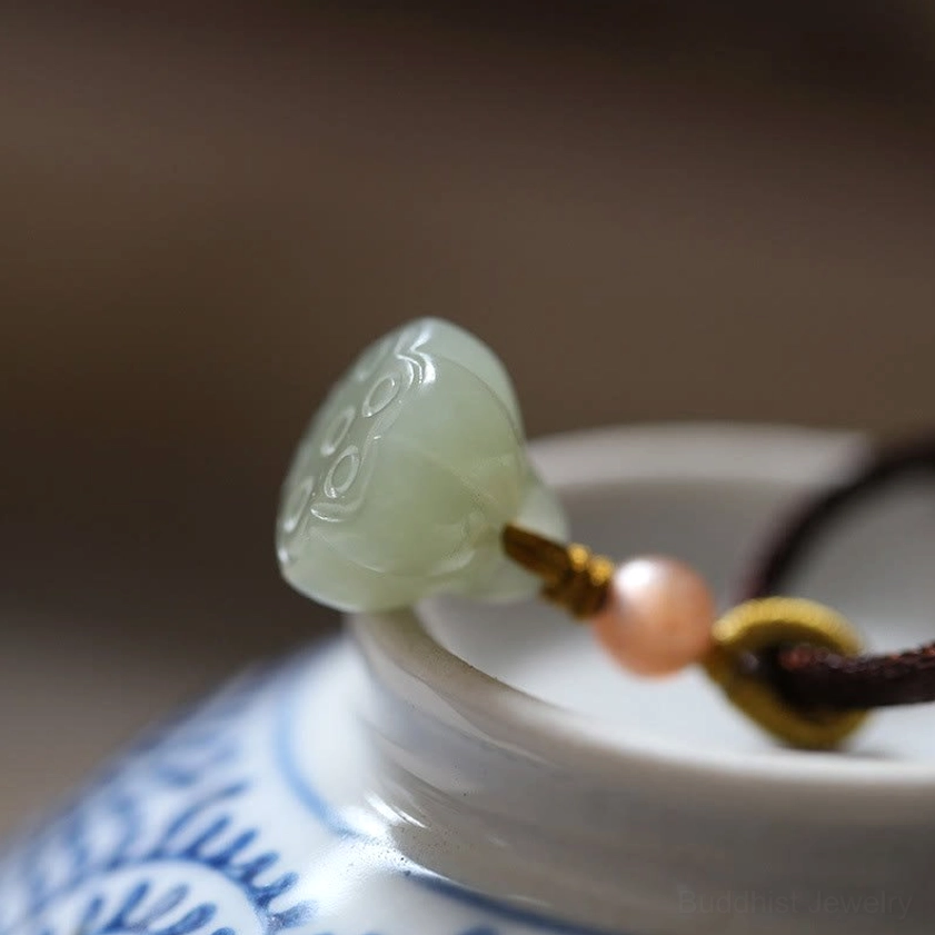 Carved light green jade lotus flower pendant on brown knotted cord close-up side view