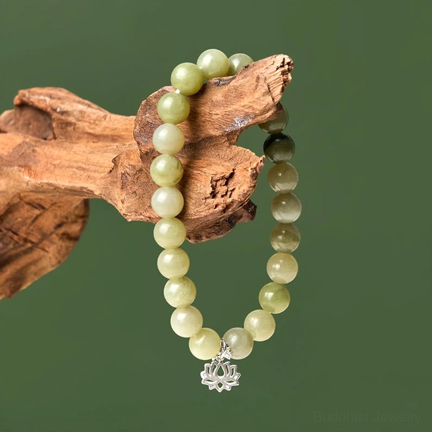 Close-up side view of cyan jade bracelet with gradient green beads and sterling silver lotus charm on wooden background