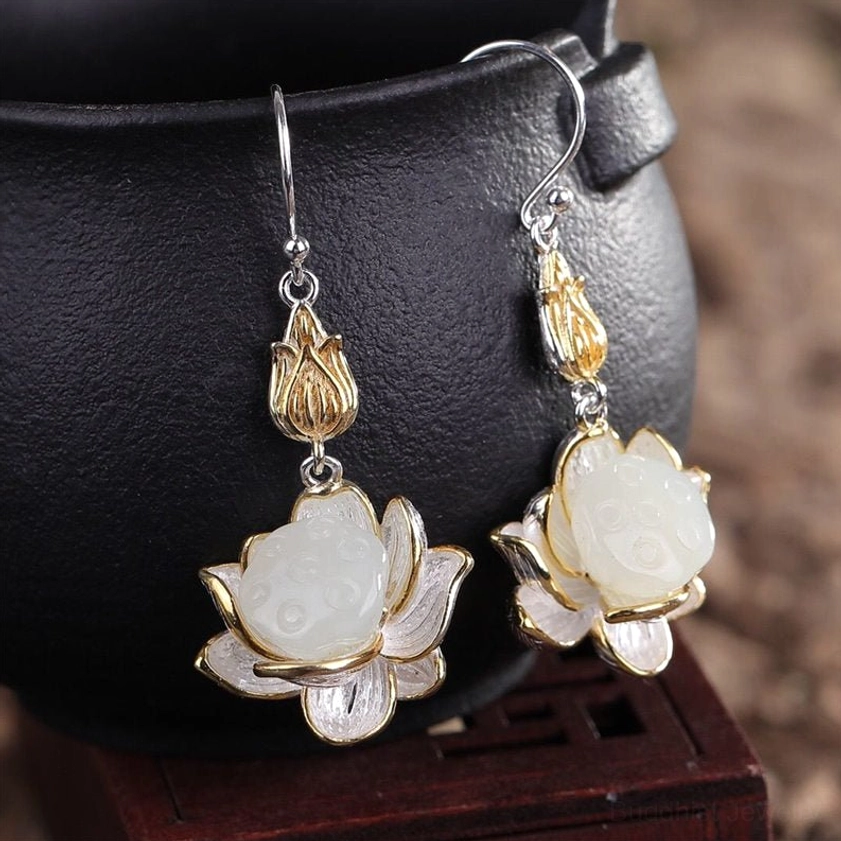 Close-up side view of white jade lotus drop earring on black ceramic display showing polished creamy jade and sterling silver ear wire