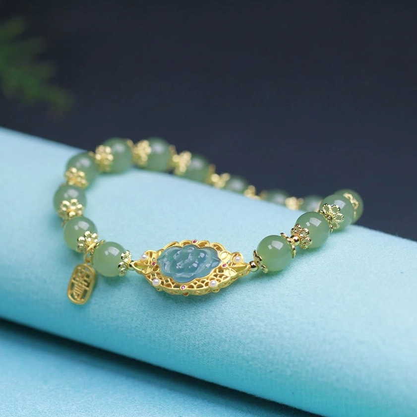 Buddhist jade lotus bracelet side view on light blue fabric, featuring matte green jade beads, gold filigree lotus charm, and hanging luck pendant