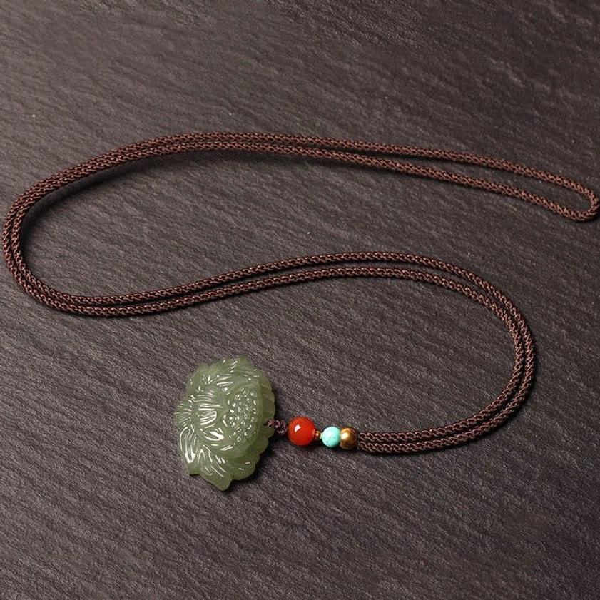 Complete Hetian jade lotus pendant necklace laid flat top-down view with brown cord and mixed accent beads on dark slate desktop background