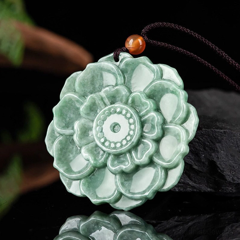 Jade lotus flower necklace pendant shown from three-quarter angle on dark reflective surface, detailed carved petal design