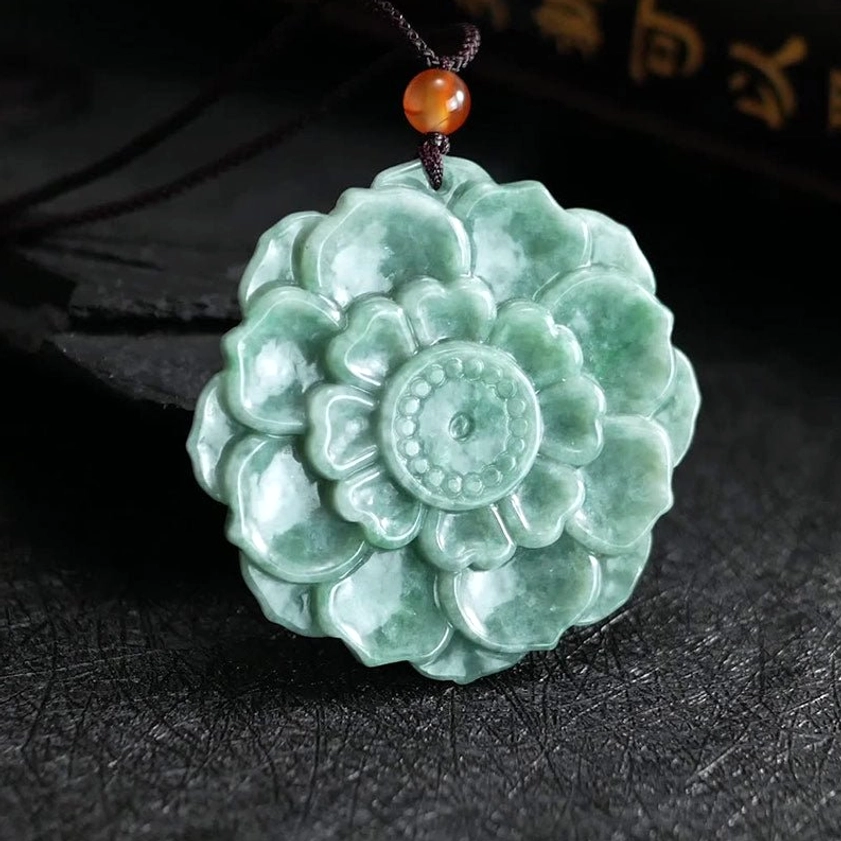 Side view of green jade lotus necklace pendant showing depth of carving and brown cord with orange accent bead