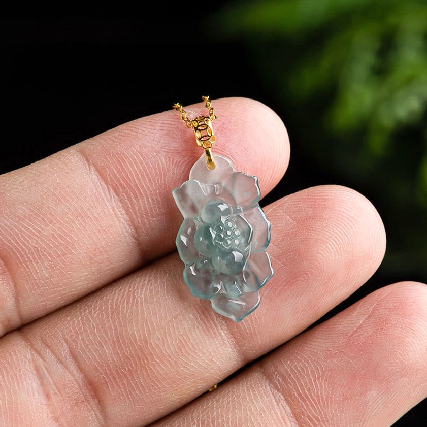 Close-up of delicate jade lotus pendant held on fingertip showing miniature carved lotus bloom and thin gold-toned chain link