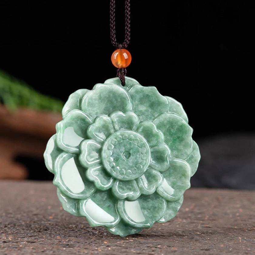 Overhead flat lay of carved green jade lotus pendant with layered petal design on wooden studio background