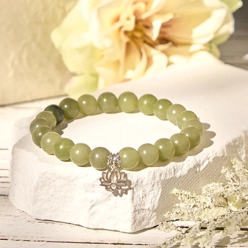 Handmade cyan jade Buddhist bracelet with silver lotus charm arranged with dried flowers and warm ambient lighting
