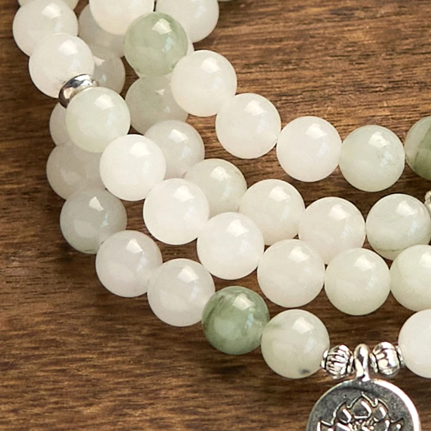 Overhead close-up of jade mala bracelet beads with silver metal spacers and engraved lotus pendant detail