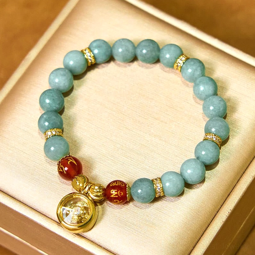 Spiritual jade bracelet with rotating Om Mani Padme Hum gold charm, crystal-set gold spacers, and round pendant on beige jewelry box background