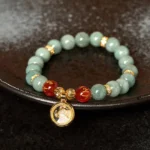 Green jade Om Mani Padme Hum spinning charm Buddhist bracelet top view with rotating gold pendant and red engraved agate beads on ceramic surface