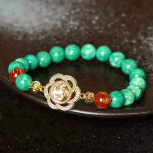 Green jade Om Mani Padme Hum rotating cyclone charm bracelet with red agate beads on dark ceramic plate