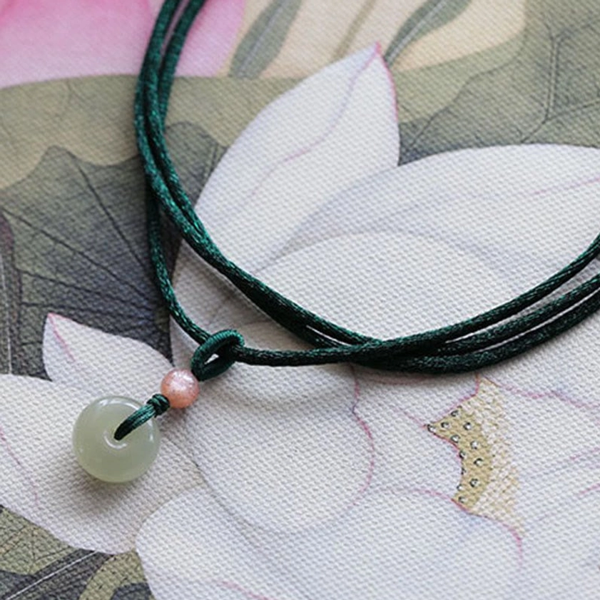 Jade peace buckle necklace flat lay on lotus flower painted background with dark green cord