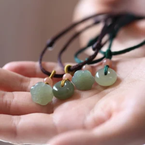 Assorted natural jade peace buckle and lotus necklace pendants displayed on palm with brown and green cords