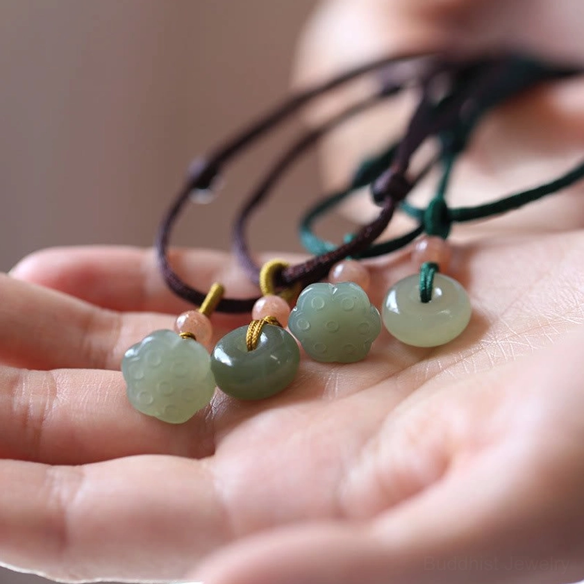 Assorted natural jade peace buckle and lotus necklace pendants displayed on palm with brown and green cords