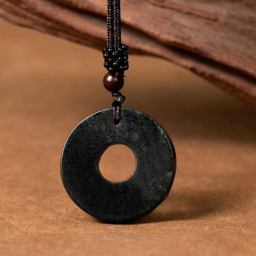 Smooth uncarved black-green jade peace buckle necklace with dark braided cord on wooden background