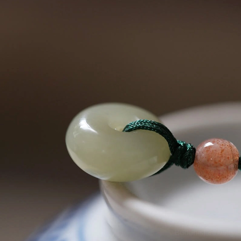 Close-up side view of polished light green jade peace buckle pendant on dark green knotted cord