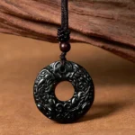 Black-green jade Pixiu peace buckle necklace with carved details and brown braided cord on wooden display