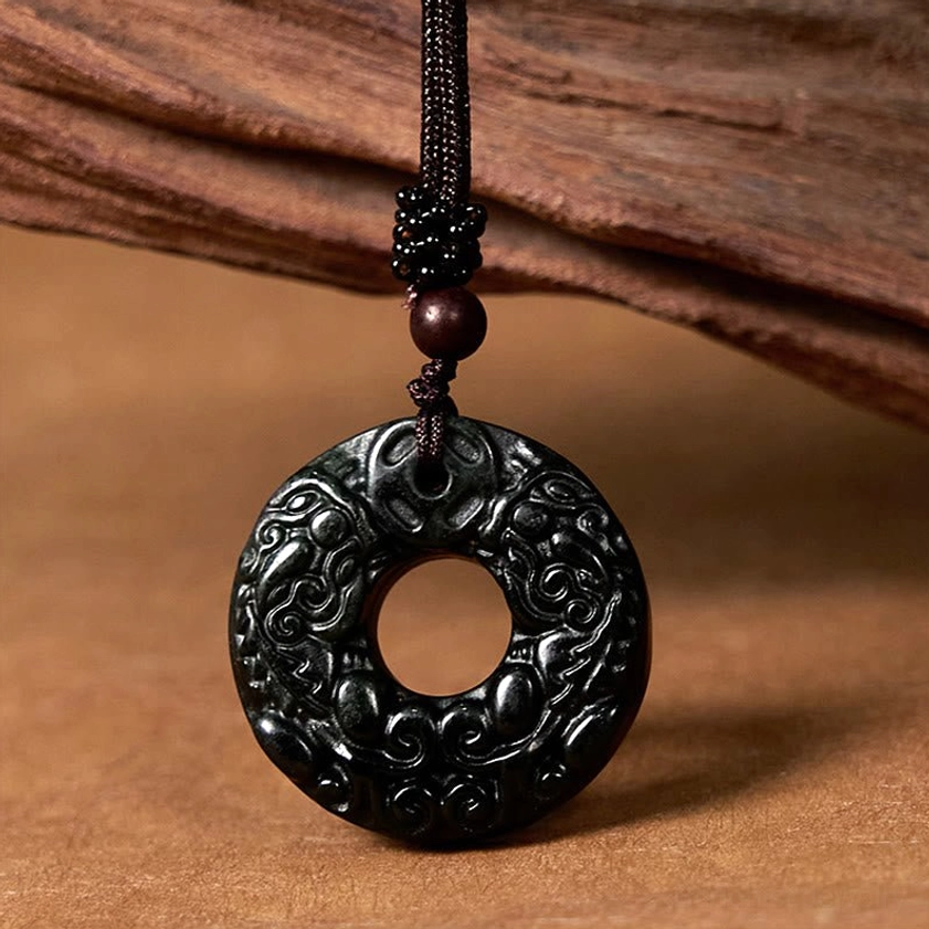 Black-green jade Pixiu peace buckle necklace with carved details and brown braided cord on wooden display
